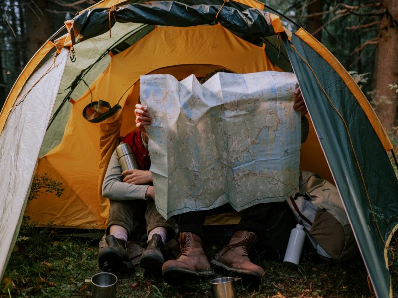 Two people enjoy a camping trip, examining a map inside a tent surrounded by nature.
